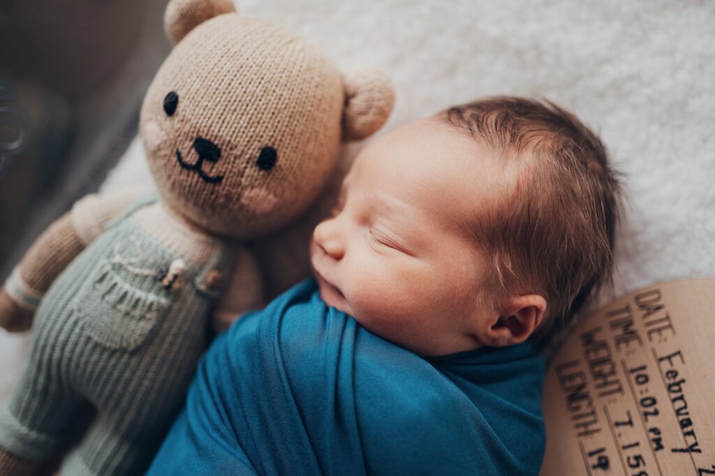 Newborn baby laying next to teddy bear in bassinet
